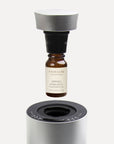An instructional view of a 10ml spring hyacinth essential oil bottle screwing into a black nozzle attachment above a silver waterless diffuser.