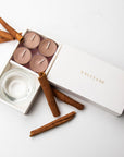 Top-down minimalist flat lay of the open cinnamon tealight candle set styled beautifully with raw cinnamon sticks on a seamless white surface.