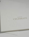 Angled top-down shot of the premium minimalist white celebration note card highlighting its crisp gold lettering and fine embossed border details.