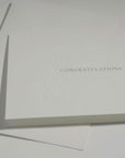 Side angle close-up emphasizing the crisp typography and premium embossed floral framework on a luxury wedding or corporate congratulations card.