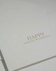 Side angle close-up showing the crisp typography and premium blind-embossed floral framework of a luxury new home congratulations card.