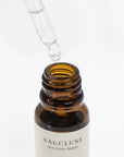 A clear glass pipette dropper hovering above an open amber glass bottle of grapefruit cedar essential oil.