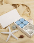 Elegant coastal lifestyle scene showing the light blue breeze tealight aromatherapy gift set styled on draped beige linen with a white starfish.