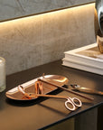 An elegant rose gold candle care set arranged on its matching tray resting on a sleek dark modern desk.