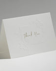 An elegant, freestanding white thank you card showcasing a delicate blind-embossed floral frame around elegant central script text.