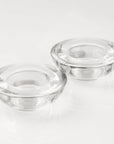 A close-up studio shot of two empty, thick clear glass tealight candle holders showcasing their heavy, high-quality round structure.