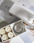 Aesthetic top-down view of the premium white musk scented tealight candle gift box arranged over editorial style design books and magazines.
