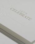 Close-up macro shot highlighting the heavy textured cotton paper and fine gold metallic lettering on the Vaucluse luxury Let's Celebrate card.