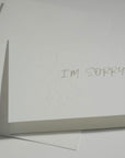 Side angle close-up focusing on the elegant embossed floral framework around the "I'm Sorry" text on premium white cardstock.