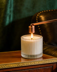 A modern rose gold bell candle snuffer being used to safely extinguish a burning candle flame on a wooden desk.