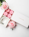 Top-down minimalist flat lay of the open pink rose tealight candle set beautifully accessorized with fresh pink rose blossoms on a white background.
