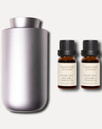 A sleek matte silver waterless nebulizing aroma diffuser positioned next to a pair of 10ml Vaucluse wood sage sea salt essential oil bottles.