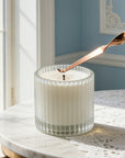 Adjusting a candle wick using a polished rose gold candle wick dipper tool on a round marble tabletop.
