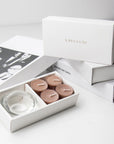 Premium unboxing scene showing the open cinnamon candle holder set placed against a neat arrangement of stacked white gift boxes with gold branding.