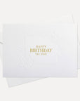 Overhead view of a minimalist luxury white birthday greeting card featuring gold foil text "Happy Birthday To You" paired with a matching white paper envelope.