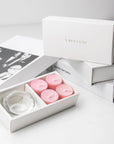 Luxury retail unboxing display showing the open pink rose candle holder set resting against stacked white gift boxes with gold foil branding.