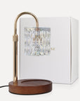 Vaucluse Fragrance premium transparent crystal candle warmer lamp with a clear glass shade, curved gold neck, and dark wood base sitting next to its white brand box.