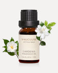 A 10ml amber glass bottle of Vaucluse Gardenia Essential Oil decorated with blooming white gardenia flowers and green leaves.