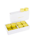 An open luxury white Vaucluse gift box displaying a set of bright yellow lemon scented tealight candles.