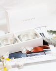 Stylized lifestyle flat lay showing the premium white Vaucluse candle holder gift box paired with elegant white flowers and an open lifestyle magazine.
