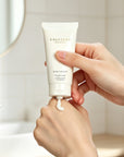 Woman squeezing a dollop of Vaucluse Rose Velvet hand cream onto the back of her hand in a brightly lit bathroom.