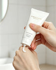 Woman squeezing a dollop of Vaucluse Rose Velvet hand cream onto the back of her hand in a brightly lit bathroom.