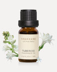 A 10ml amber glass bottle of Vaucluse Tuberose Essential Oil, accented by elegant white tuberose flower blossoms and green stems.