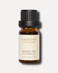 A professional studio shot of a 10ml amber glass bottle of Vaucluse White Tea Essential Oil featuring a textured black screw cap.