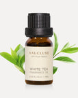 A 10ml amber glass bottle of Vaucluse White Tea Essential Oil with fresh, vibrant green tea leaves sprouting behind it.