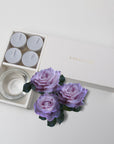 Minimalist top-down flat lay of the open velvet tealight candle set beautifully accessorized with three dusty purple rose blossoms on a white surface.