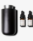 A sleek black and silver waterless nebulizing diffuser standing next to two amber glass essential oil bottles with black droppers.