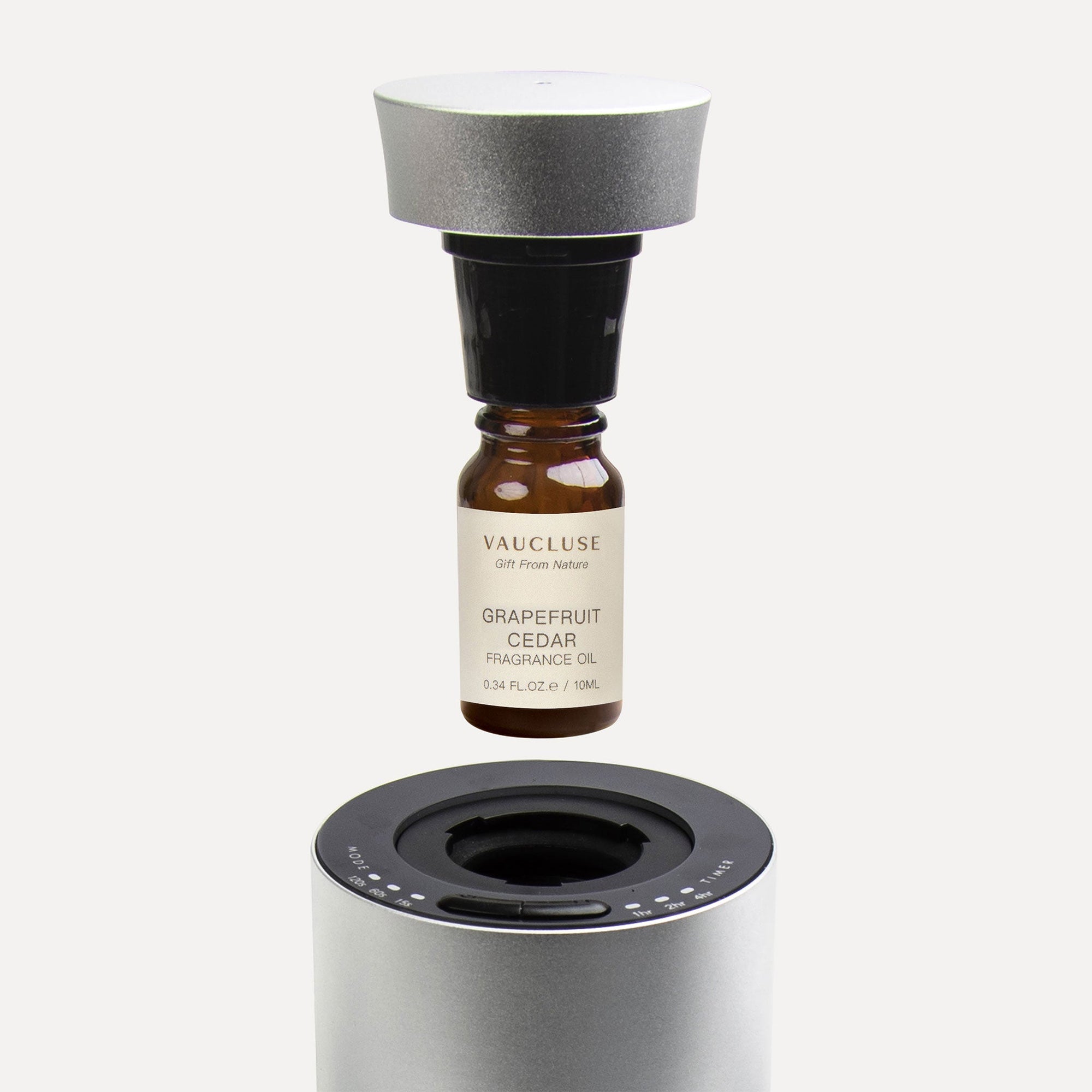 An instructional view of a 10ml Vaucluse grapefruit cedar essential oil bottle connecting to a black nozzle cap above a silver waterless diffuser.