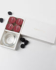Minimalist overhead flat lay of the open dark red tealight candle set styled with scattered fresh ripe blackberries on a clean white background.