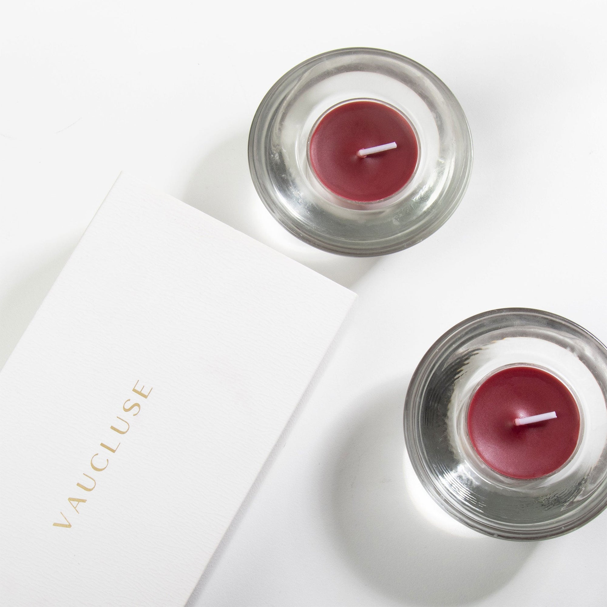 A premium white Vaucluse 16-pack box sliding open to reveal the top tier of deep purple blackberry tealight candles, elegantly styled with rich dark berries.