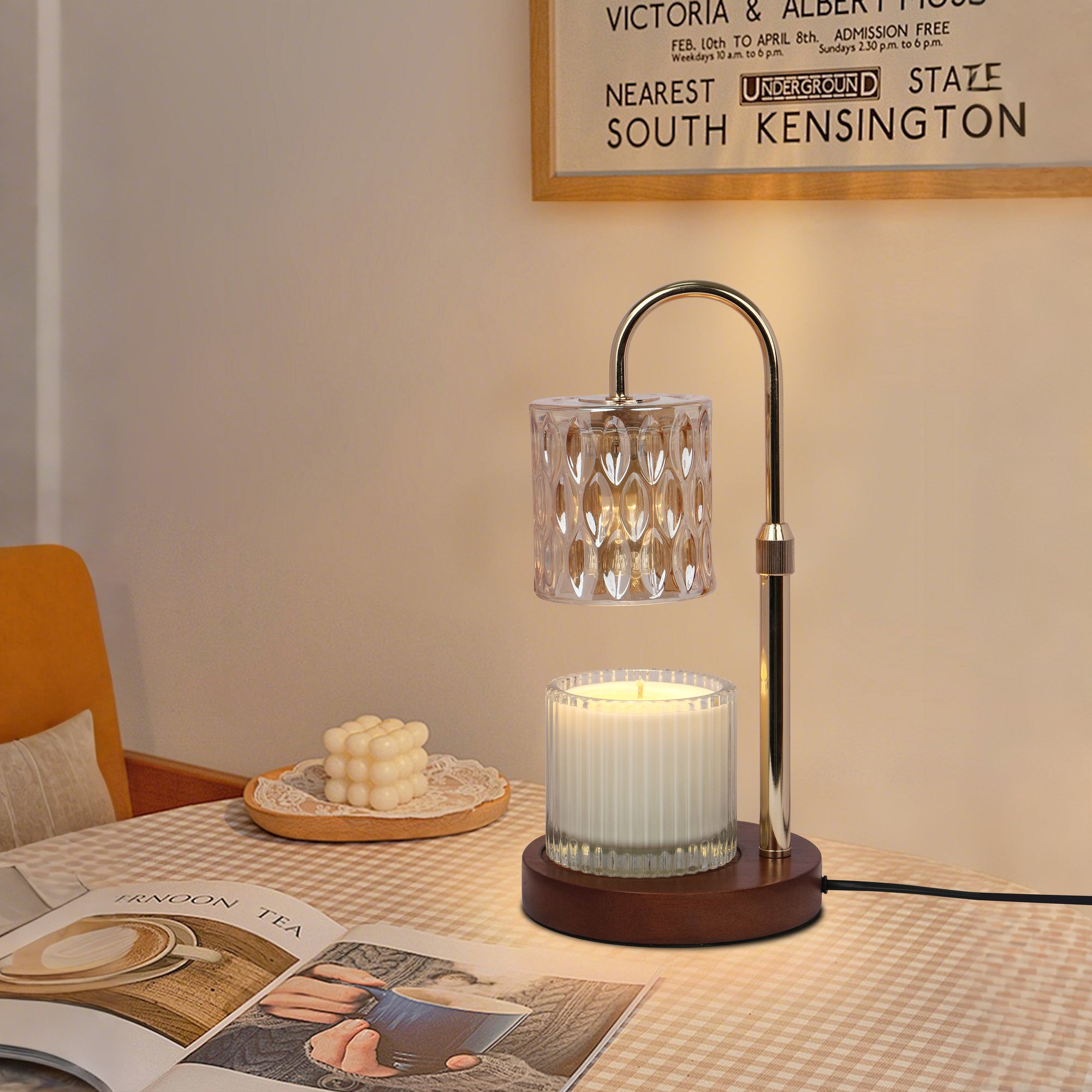 A lit crystal candle warmer lamp casting a warm amber glow over a jar candle on a bedside table with a striped tablecloth.