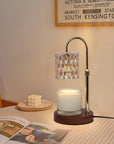 A lit crystal candle warmer lamp casting a warm amber glow over a jar candle on a bedside table with a striped tablecloth.