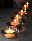 A sequential row of lit tealight candles in clear glass decorative holders fading out into a warm, soft golden bokeh background.