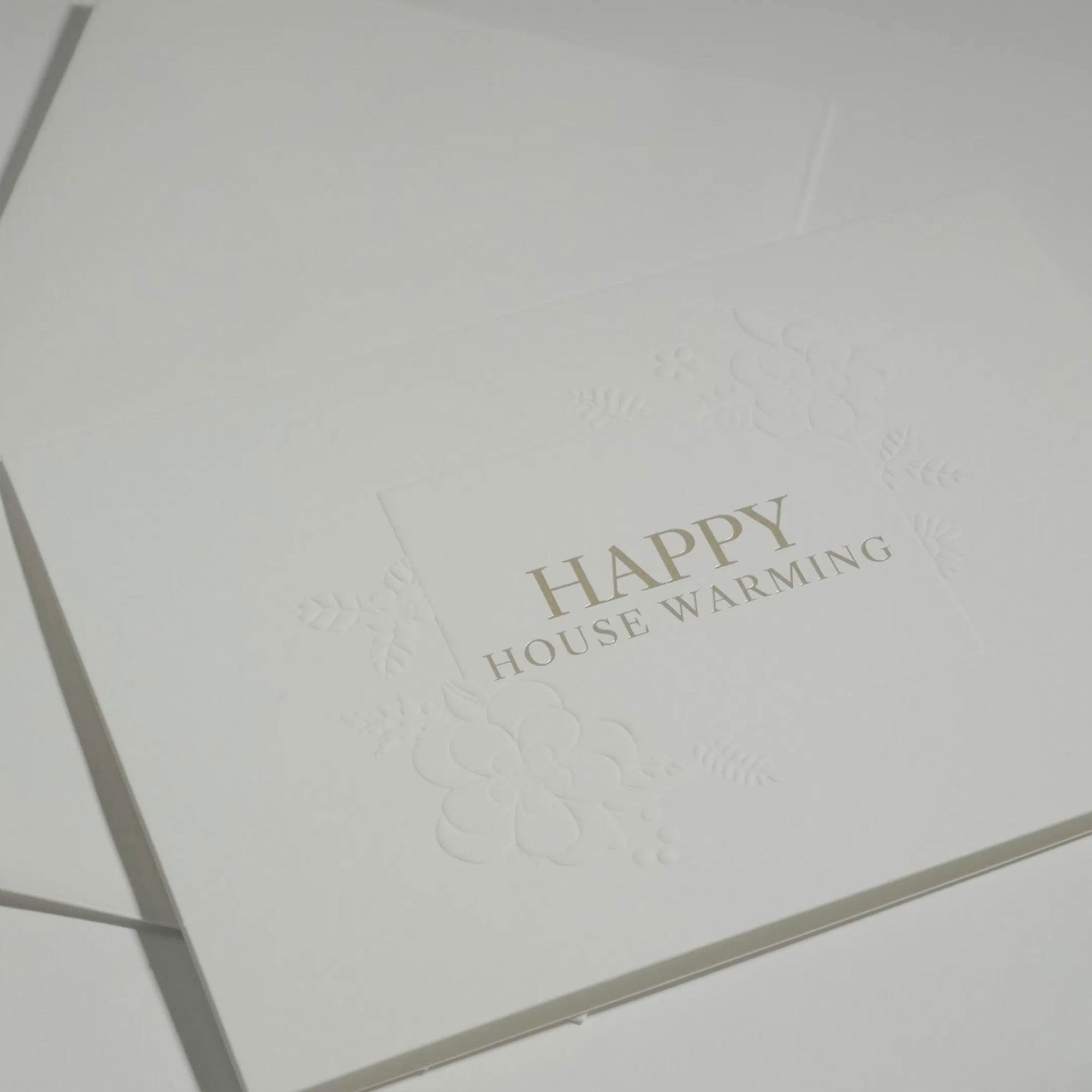 Side angle close-up showing the crisp typography and premium blind-embossed floral framework of a luxury new home congratulations card.