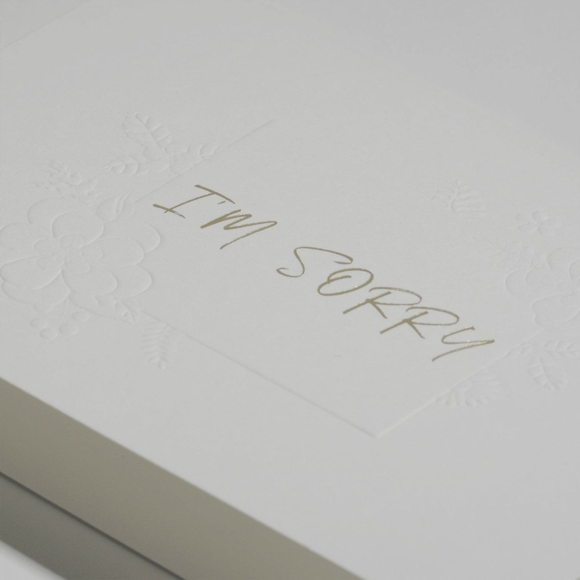 Close-up macro view showing the textured white cardstock and fine debossed details of the elegant "I'm Sorry" apology message.
