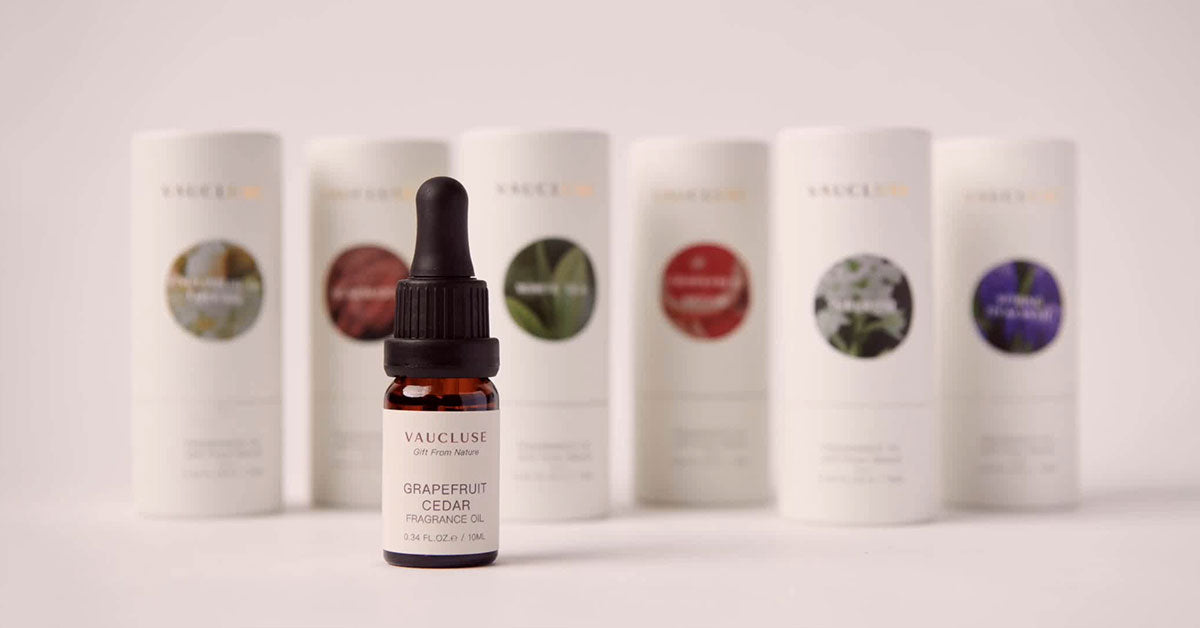 Vaucluse Grapefruit Cedar fragrance oil bottle with a dropper standing in front of a row of assorted Vaucluse essential oil canisters.