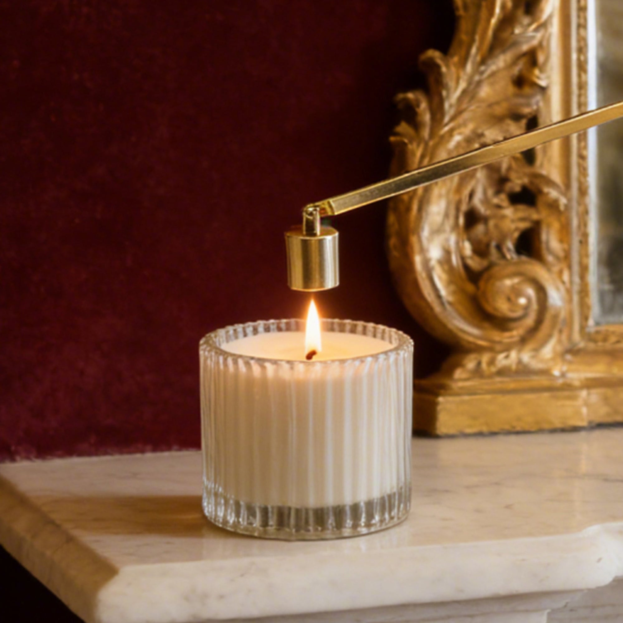 A classic gold bell candle snuffer being used to safely extinguish a burning candle flame on a mantlepiece.