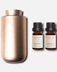 A sleek rose gold waterless nebulizing aroma diffuser displayed with two 10ml Vaucluse amber bottles of bergamot essential oil.
