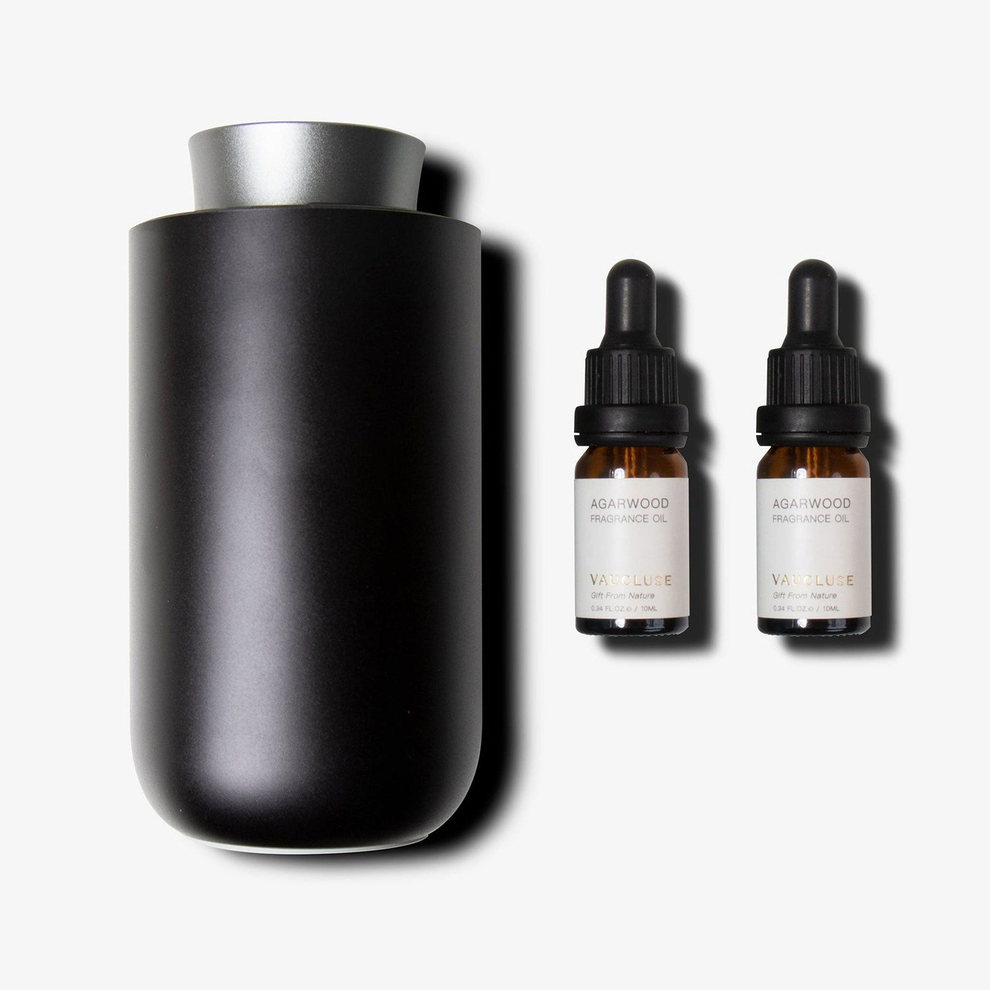 A dark gun metal waterless nebulizing diffuser standing next to two amber glass essential oil dropper bottles with black caps.