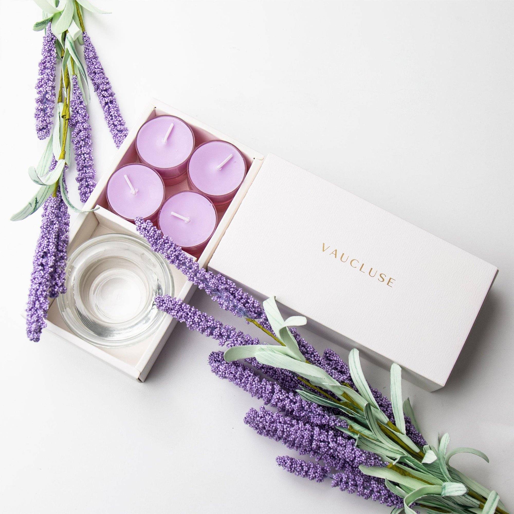 Top-down minimalist flat lay of the open lavender tealight candle set beautifully decorated with purple lavender faux stems on a seamless white backdrop.