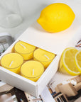 Close-up view of the premium white Vaucluse sliding packaging revealing a tiered 16-pack tray of yellow lemon scented tealight candles styled next to a whole lemon and fresh slices.