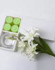 Minimalist top-down flat lay of the open green lily tealight candle set styled beautifully with fresh white lily flowers on a seamless white backdrop.