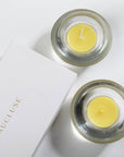 An overhead top-down view of yellow lemon scented tealight candles in clear glass holders next to a white Vaucluse luxury gift box.