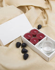 Elegant lifestyle scene showing the deep plum blackberry tealight aromatherapy gift set styled on draped beige linen fabric with fresh blackberry accents.
