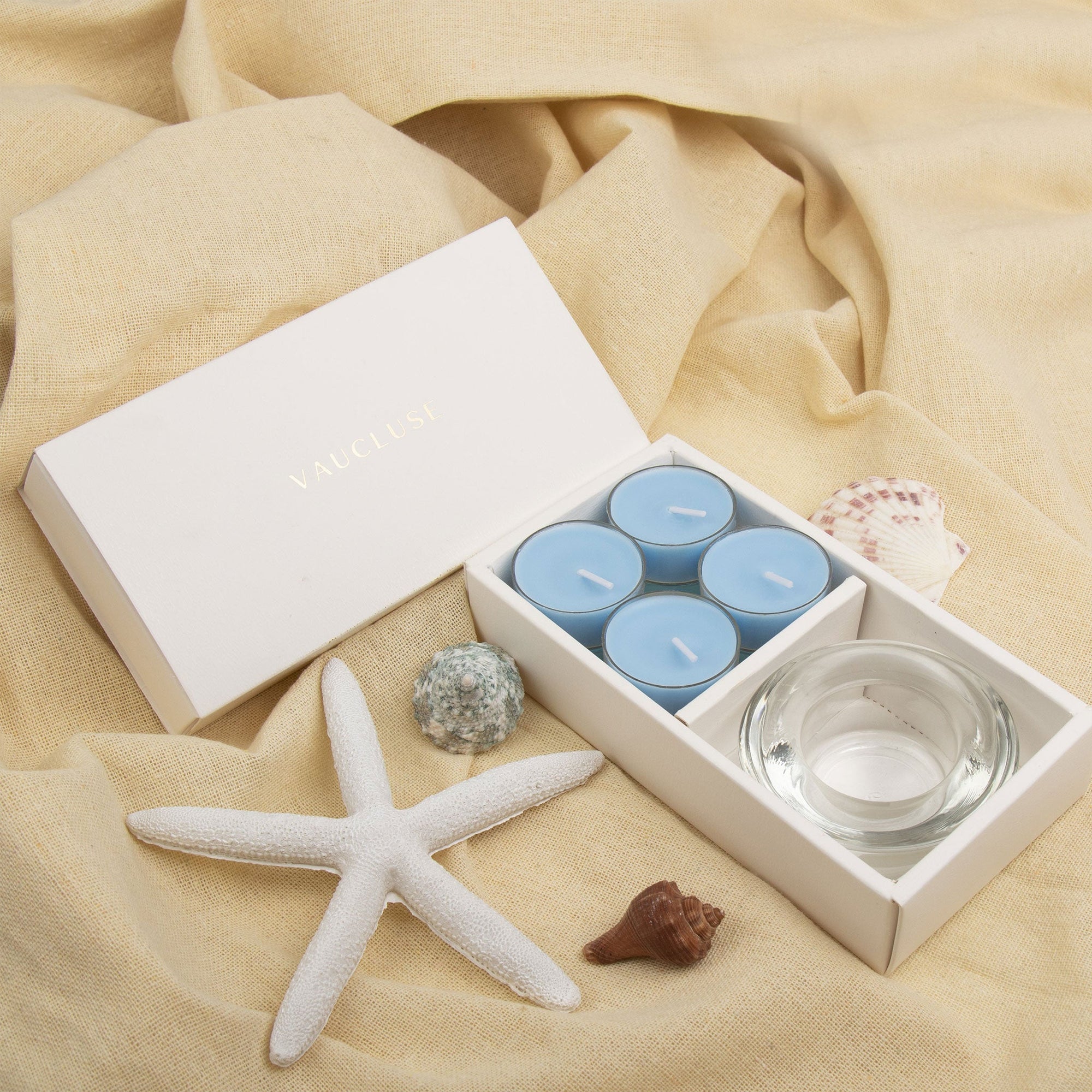 Elegant coastal lifestyle scene showing the light blue breeze tealight aromatherapy gift set styled on draped beige linen with a white starfish.
