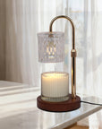 A lit transparent crystal candle warmer lamp casting a warm glow while melting a jar candle on a polished white marble tabletop.